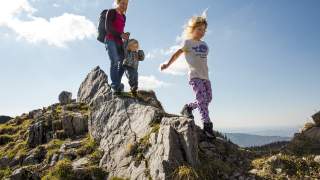 Mutter mit ihrem zwei Kindern auf einem Felsvorsprung in den Bergen.