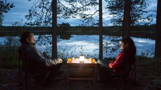 Zwei Menschen sitzen abends am See, mit Kerze und Bier.