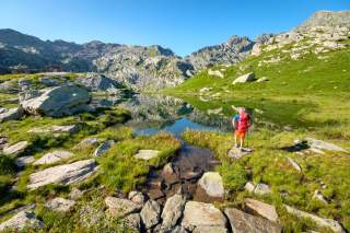 Wanderer vor Bergsee mit Wiesen und Felsen
