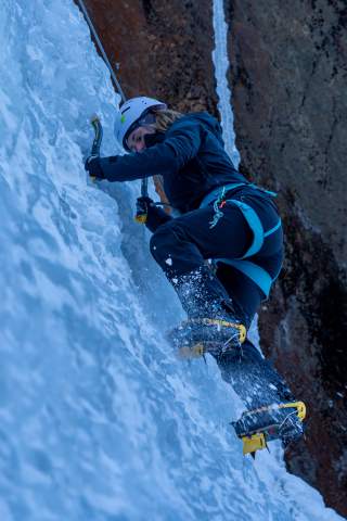 Frau beim Eisklettern. Mit Steigeisen und Eispickeln geht es Stück für Stück den gefrorenen Wasserfall hinauf.