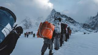 Viele Menschen tragen Fässer und andere schwere Pakete, stapfen durch den Schnee zum nächsten Basislager.