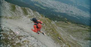 Trailrunner läuft auf schmalem Steig, im Tal sieht man eine Stadt