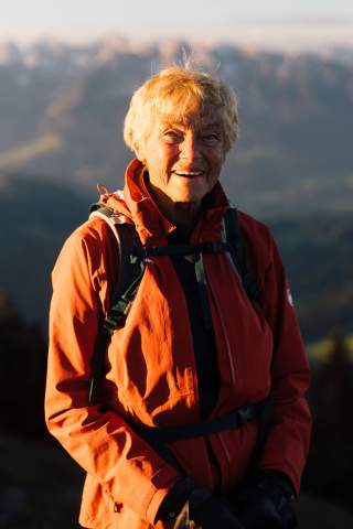 Seniorin steht in den Bergen und lächelt in die Kamera