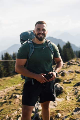 Ein Mann steht in den Bergen, er lächelt in die Kamera