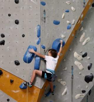 Ein Kind klettert gesichert an einer bunten Indoor-Kletterwand.