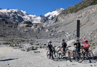 Vier Kinder auf Mountainbikes stehen in Gebirgslandschaft vor Gletscher