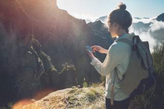 Junge Frau nutzt ihr Smartphone während einer Bergtour.