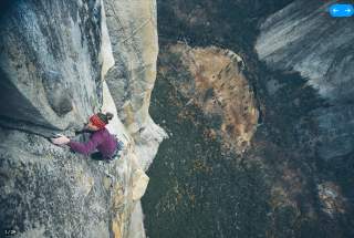 Kletterin mit rotem Stirnband klettert eine steile Felswand hinauf, weit über dem Talboden.