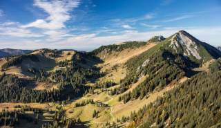 Ein Blick von oben auf den Geigelstein, der fast bis zum Gipfel von Wiesen, Wäldern und niedrigen Latschen geziert ist.