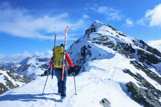 Eine Skibergsteigerin läuft die letzten Meter zum Gipfel eines schneebedeckten Berges.