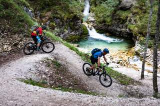 Zwei Mountainbiker befahren oberhalb eines Wasserfalls einen Trail