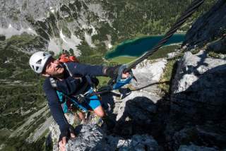 Mann in Klettersteig mit Blick ins Tal Mann in Klettersteig mit Blick ins Tal