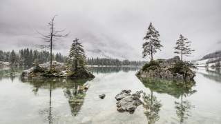 Blick auf den Hintersee und die kleinen Steininseln im See. Rundherum liegt Schnee, die Wolken liegen tief im Tal.