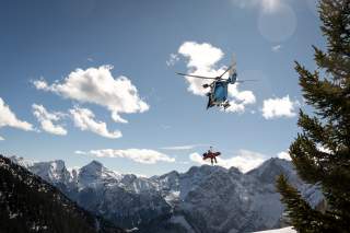 Hubschrauber in den Alpen mit geretteter Person an Seilwinde