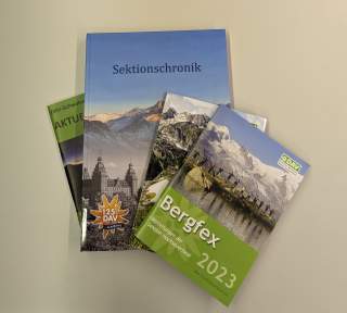 Auf einem weißen Hintergrund liegen vier verschieden große Bücher. Auf dem Cover von allen ist ein Bergmotiv zu sehen.