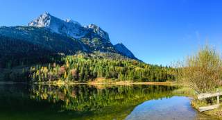 Pano-Tour Klais-Ehrwald Ein Bergsee, in dessen Wasser sich Bäume und die felsigen Gipfel spiegeln.