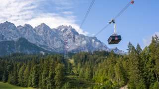 Man sieht eine sehr große Kabine der Zugspitz-Seilbahn, darunter viel Bergwald und im Hintergrund das Panorama des zackigen Wettersteingebirges.