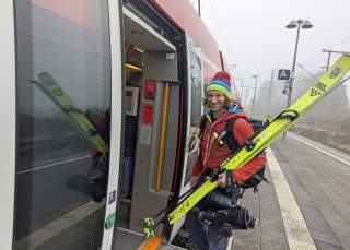 Bernhard Angerer steigt bepackt mit Skiern und Skischuhen in einen Regionalzug.