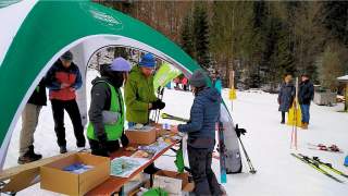 Mehrere Menschen sammeln sich um einen Infostand, der Stand steht im Schnee, im Hintergrund ist ein Bergwald zu sehen.