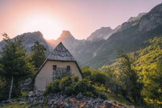 Verfallenes Haus vor hinter Berggipfeln untergehender Sonne