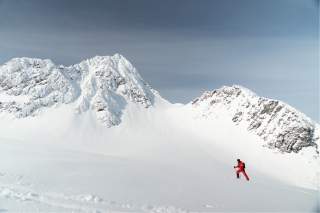Ein Skitourengeher im verschneiten Hochgebirge. Er trägt grell-rote Kleidung.