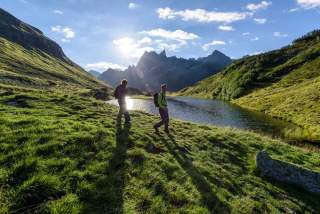 Zwei Menschen wandern an Bergsee entlang
