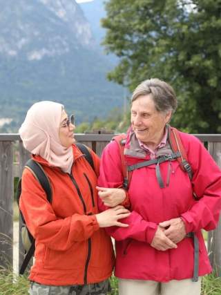 Junge Wanderin mit Kopftuch hakt sich bei einer älteren Wanderin unter.