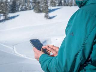 Mensch in Schneelandschaft orientiert sich mit Smartphone