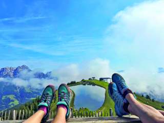 Die Schuhe zweier Wanderer, im HIntergrund ein Speicherteich und eine Bergstation.