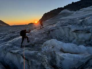 Zwei Hochtourengeher*innen auf dem Gletscher bei Sonnenaufgang.