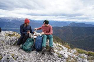 Zwei Personen sitzen am Gipfel und machen Brotzeit