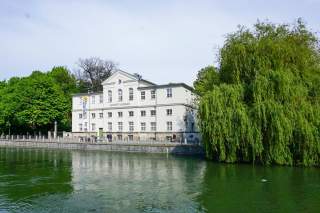 Das Alpine Museum in München an einem Frühsommertag, im Vordergrund die Isar.