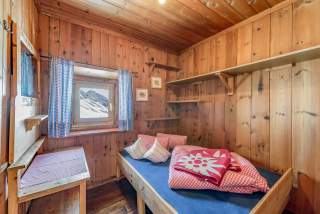 Rote-weiße Decken liegen auf dem Bett eines einfachen Schlaflagers einer Alpenhütte.