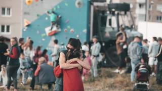 Nina Caprez umarmt ein Mädchen. Im Hintergrund ist Ninas Unimog samt Boulderwand und viele Menschen zu sehen.