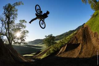Mountainbiker bei Stunt in Landschaft mit Wiesen und Bäumen