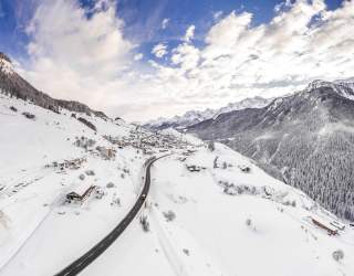 Ein Panoramablick auf das verschneite Unterengadin. Das Dorf Ardez am Berghang, dahinter hohe Berge.