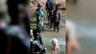 Astrid als Kleinkind in einem Fluss, umgeben von Einheimischen die mit im Wasser stehen.