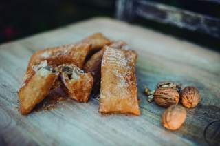 Nahaufnahme von mehreren gebackenen Teigtaschen mit Zucker bestreut auf einem Holzbrett, daneben einige Walnüsse in und außerhalb der Schale.
