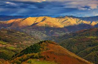Blick über ein Tal mit Bergen in intensiven Herbstfarben und gewittriger Stimmung.