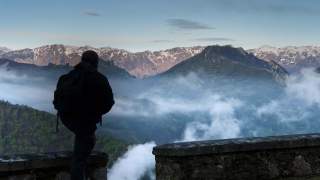 Wanderer blickt auf leicht verschneite Hochgebirgskette.