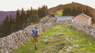 Wanderer läuft zwischen alten Steinmauern in Richtung eines verlassenen Weilers.