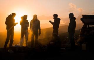 Gruppe von Menschen steht bei Sonnenuntergang am Auto