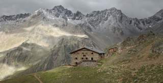 Schutzhütte aus braunen Steinen, im Hintergrund graubraune Gipfel die leicht mit Schnee bedeckt sind. Schutzhütte aus braunen Steinen, im Hintergrund graubraune Gipfel die leicht mit Schnee bedeckt sind.