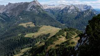 Grüne Wiesen und Wälder gehen über in hellgraue Felsgipfel, die sich aneinanderketten.