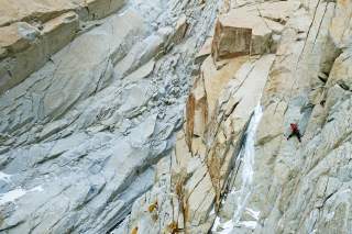 Bergsteiger mit rotem Rucksack klettert an einer steilen, eisbedeckten Felswand.