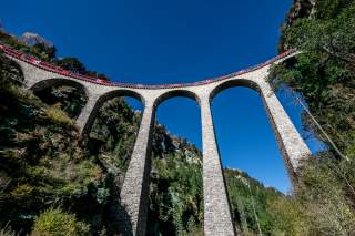 Riesige Bögen eines Viadukts reichen weit gen Himmel. Auf dem Viadukt überquert ein Zug die Schlucht.
