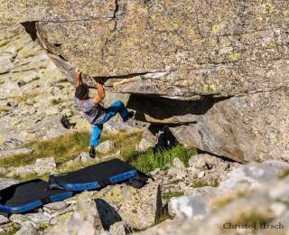 Ein Boulderer an einem Felsen, auf dem Boden Bouldermatten zum Schutz.