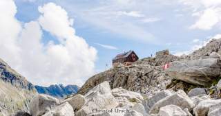 Eine Alpenvereinshütte erscheint klein in einer riesigen Geröllwüste.