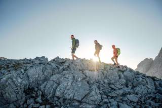 Drei Menschen wandern auf Felsen bei untergehender Sonne