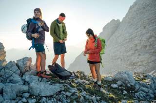 Drei Menschen am Berg ziehen nach der Pause wieder Jacken an Drei Menschen am Berg ziehen nach der Pause wieder Jacken an